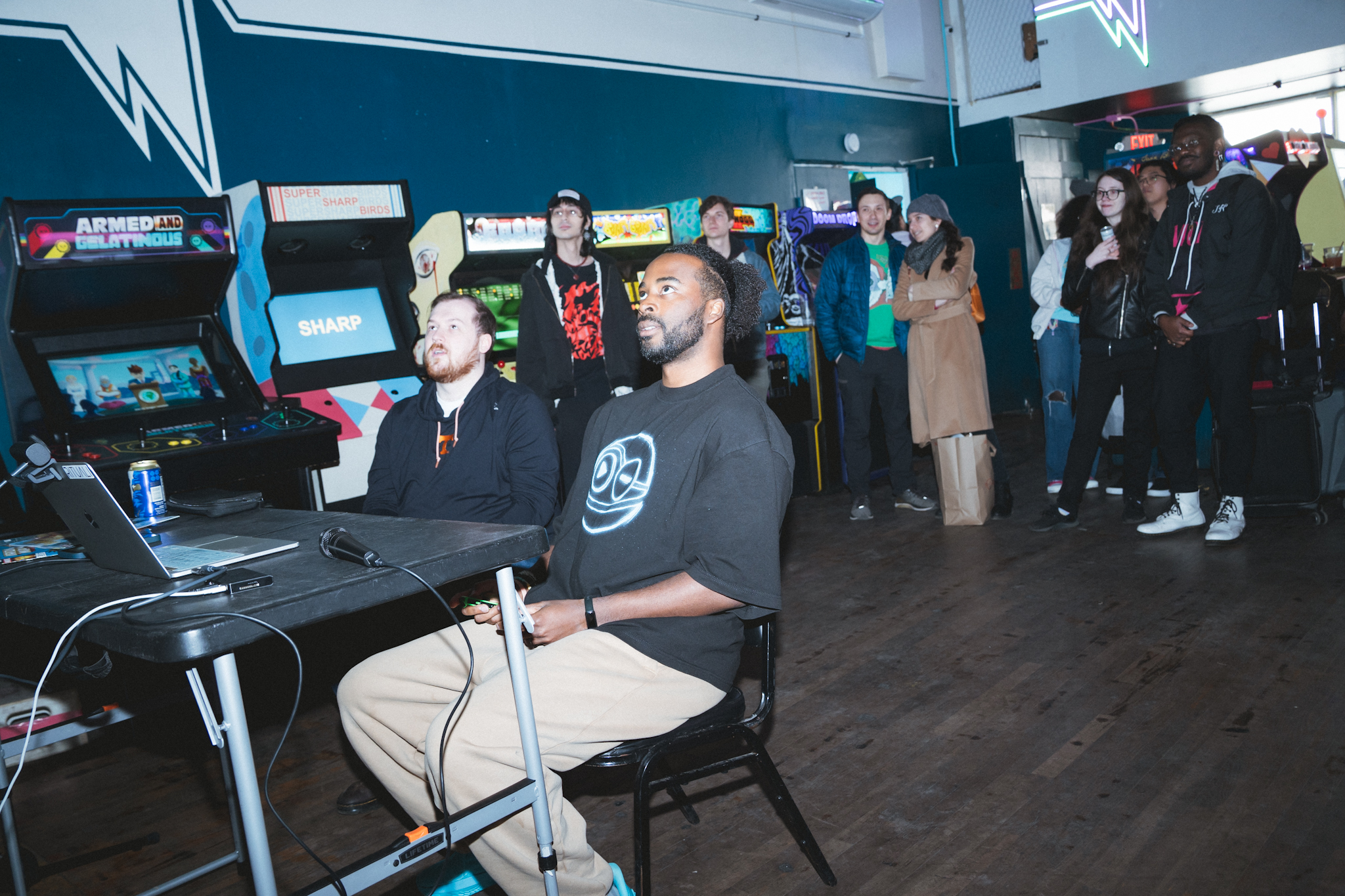 Ryan The Son seated at the arcade listening event, audience watching